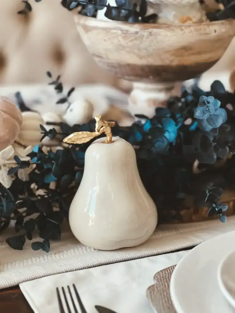 An off white ceramic pear on a table with blue eucalyptus