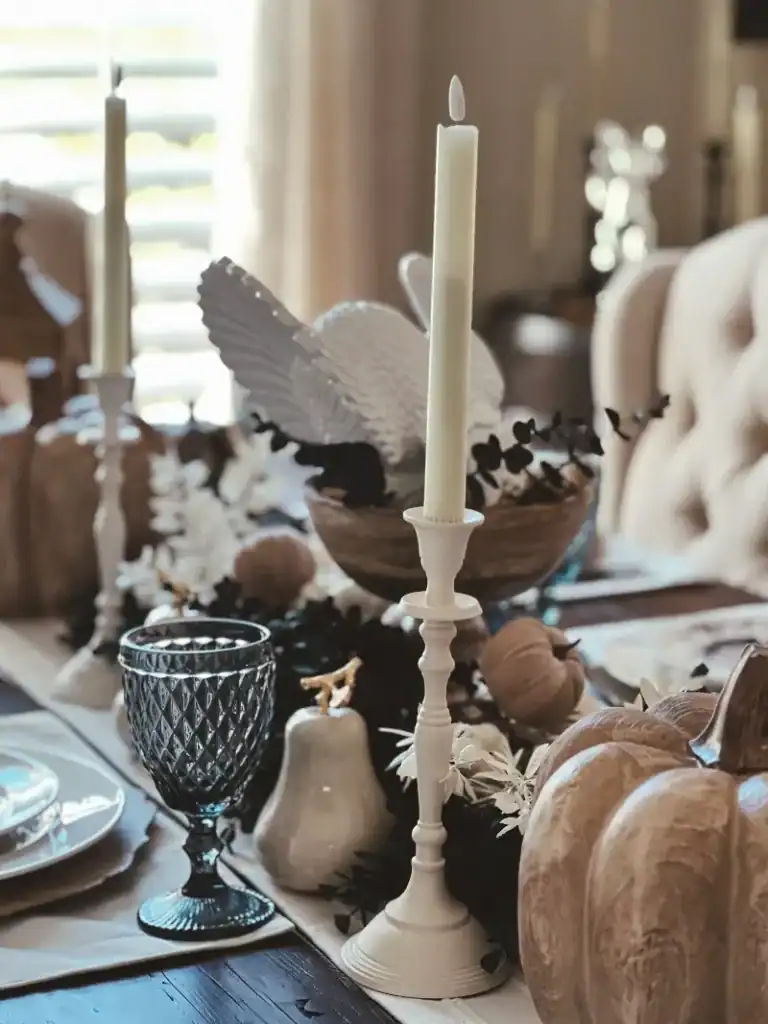 A white candlestick on a table with a blue goblet and other items blurred in the background