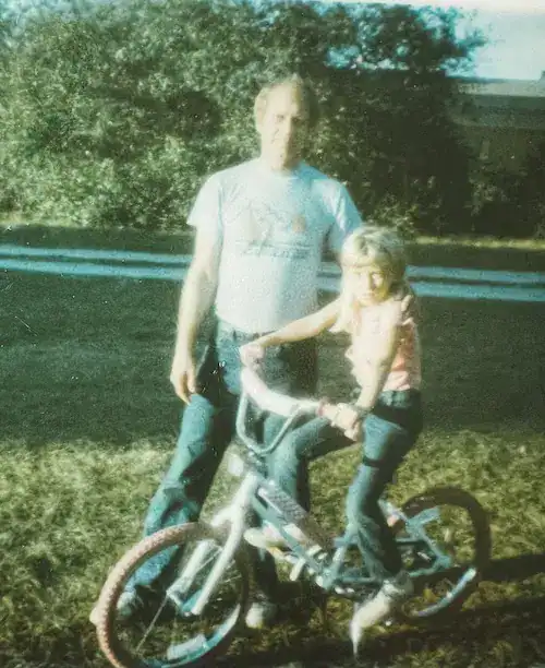 Girl on bicycle with man standing next to her with hand on shoulder