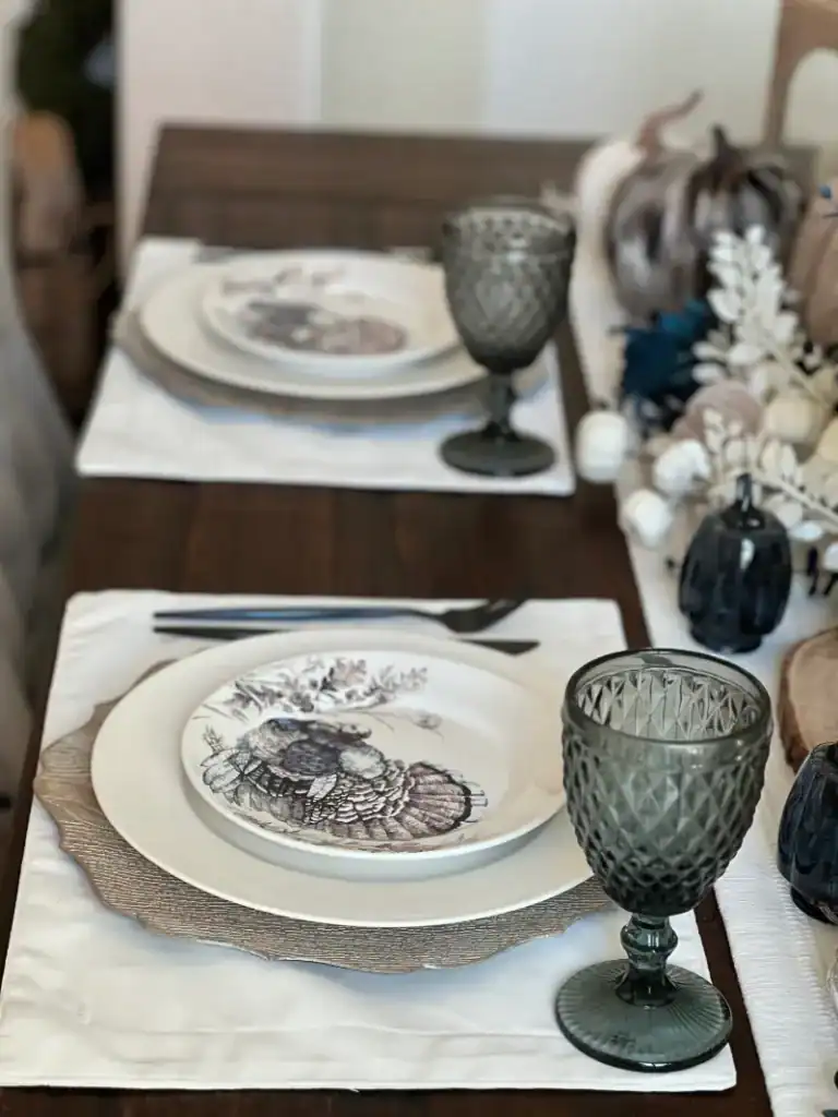 Side view of two blue and white Thanksgiving placesettings that has a turkey on the plate, blue goblets and black flatware