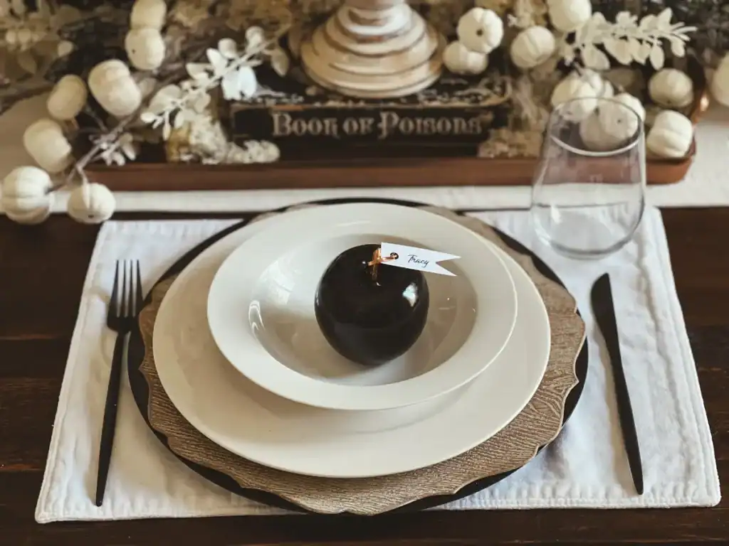 A black apple on a white pacesetting with a name tag that says Tracy for a Halloween party