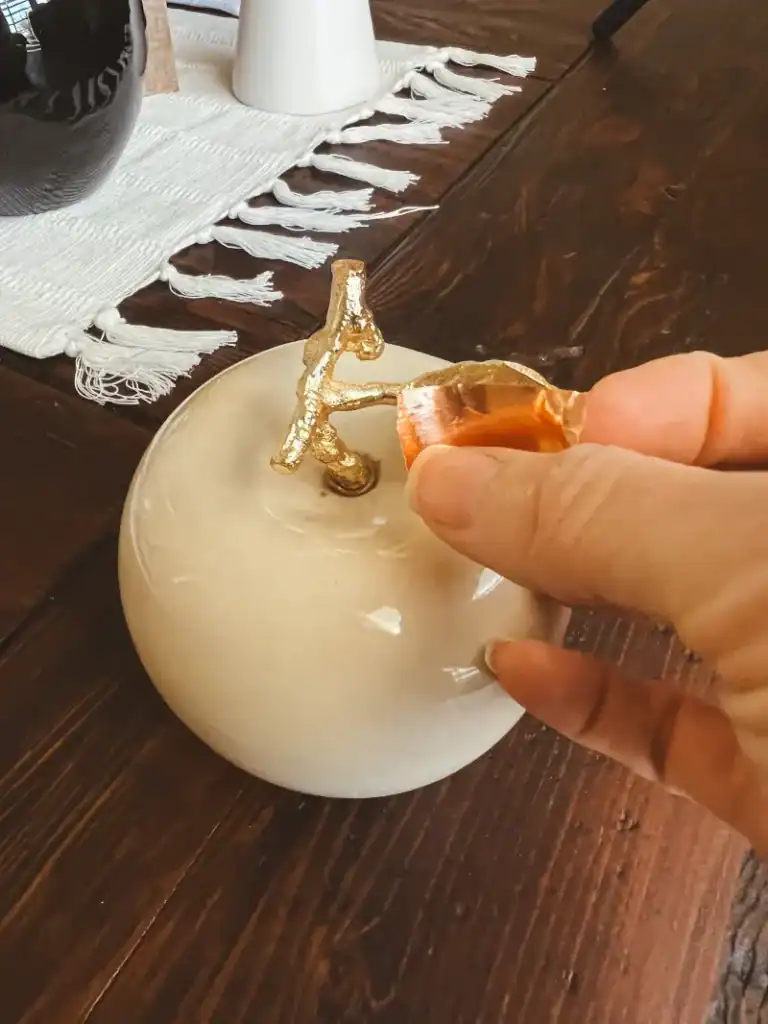 A hand is holding a piece of copper washi tape and putting it on a white apples gold leaves to change them to a copper color