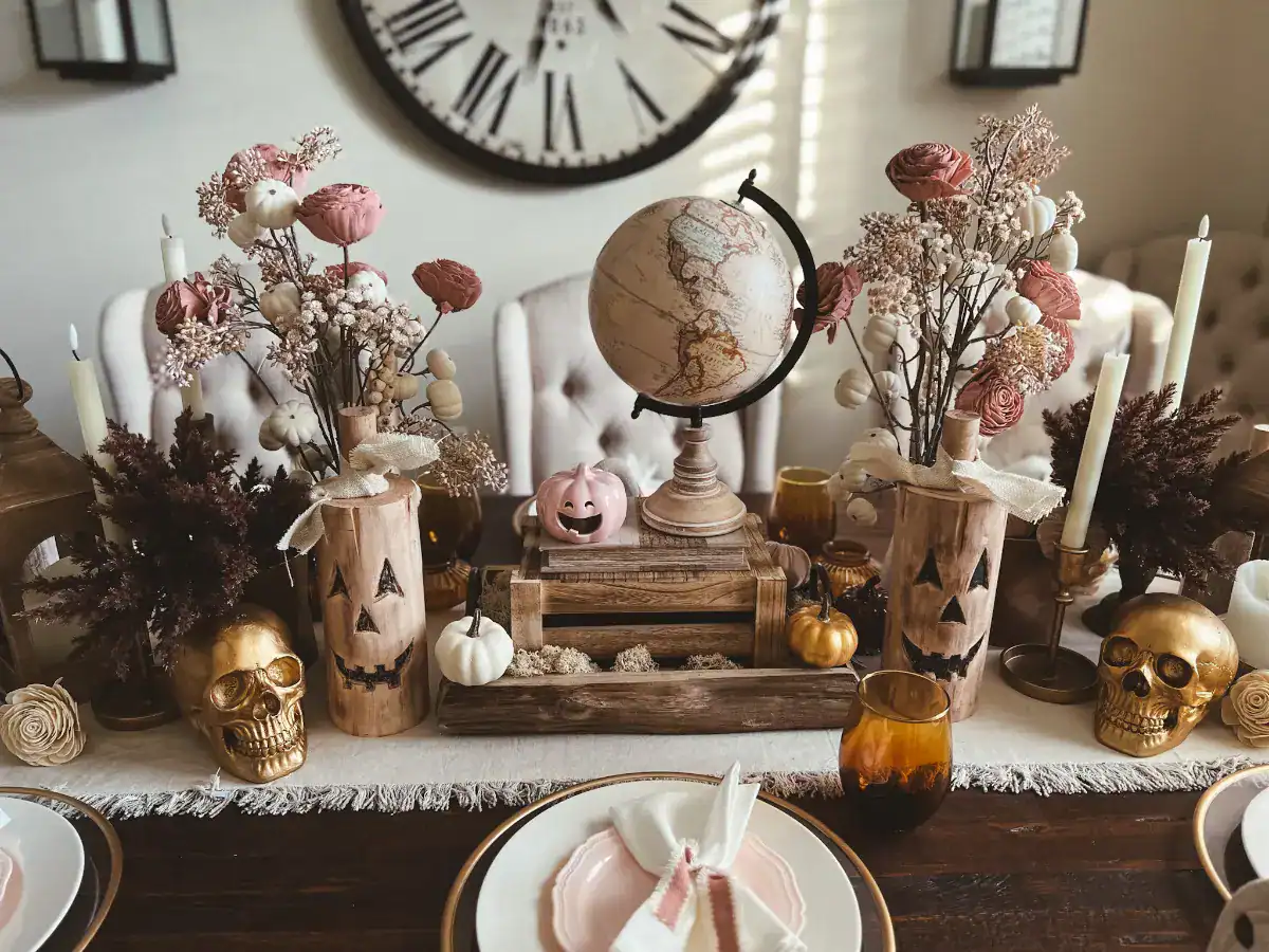 A pink, gold and wood Halloween tablescape with a beige globe, gold skulls and wood accents
