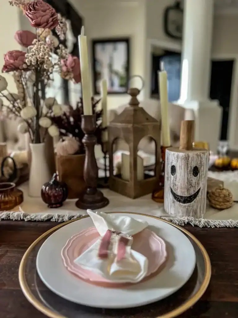 A tablescape decorated with a wood white painted ghost and a pink plate for Halloween
