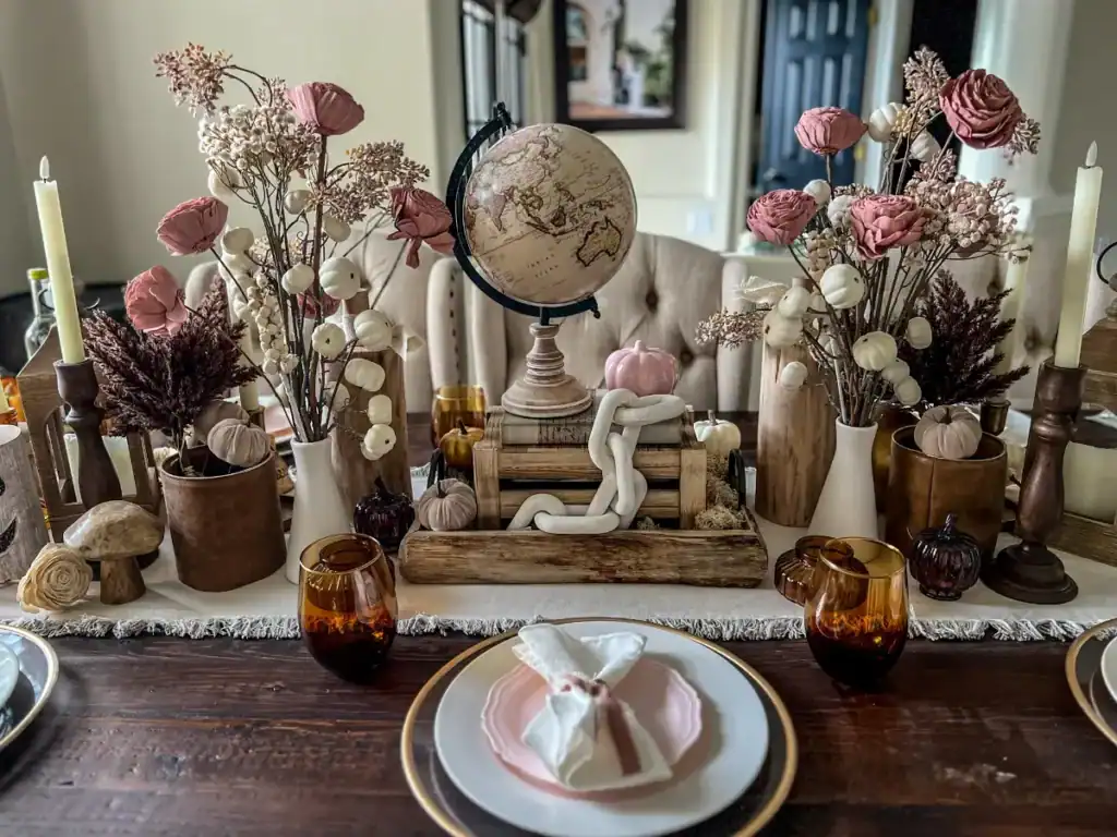 A tablescape decorated with a globe, wood and pink flower and plate accents