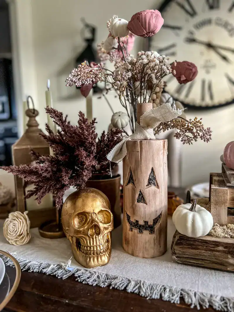 A gold skull and a carved wooden jack o lantern on a table with pink accents for a Halloween tablescape