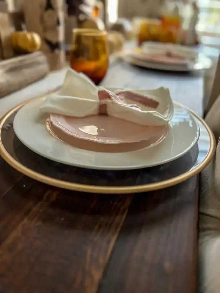 A plastic pink plate on a white plate with a charger underneath topped with a white napkin with pink ribbon