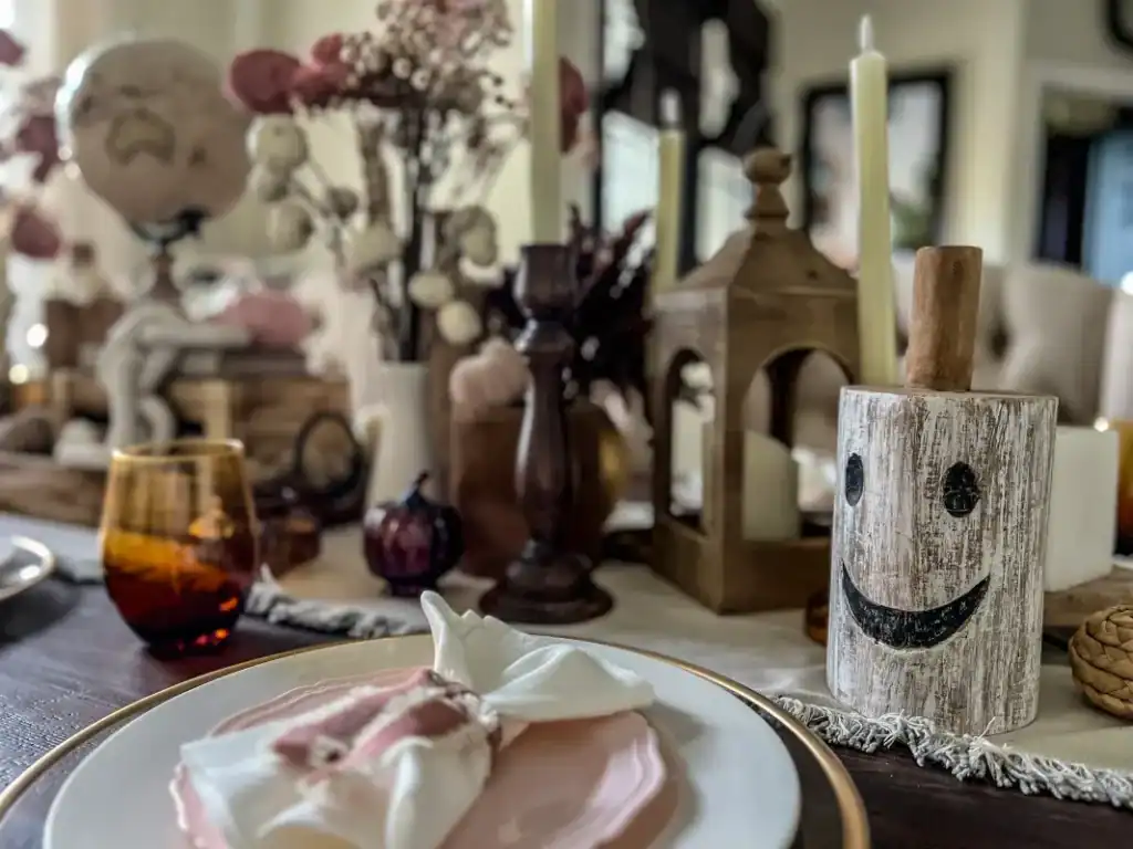 A tablescape decorated with a wood white painted ghost, candlestick and a pink plate