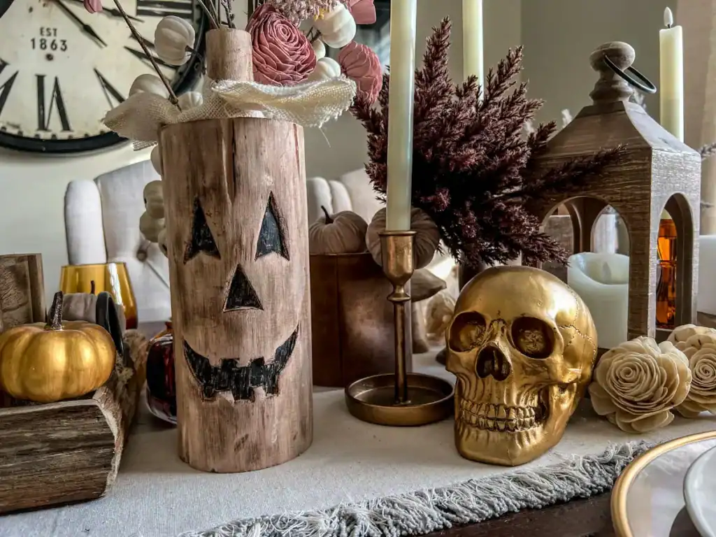 A gold skull, gold candleholder and a carved wooden jack o lantern on a table with pink accents for a Halloween tablescape