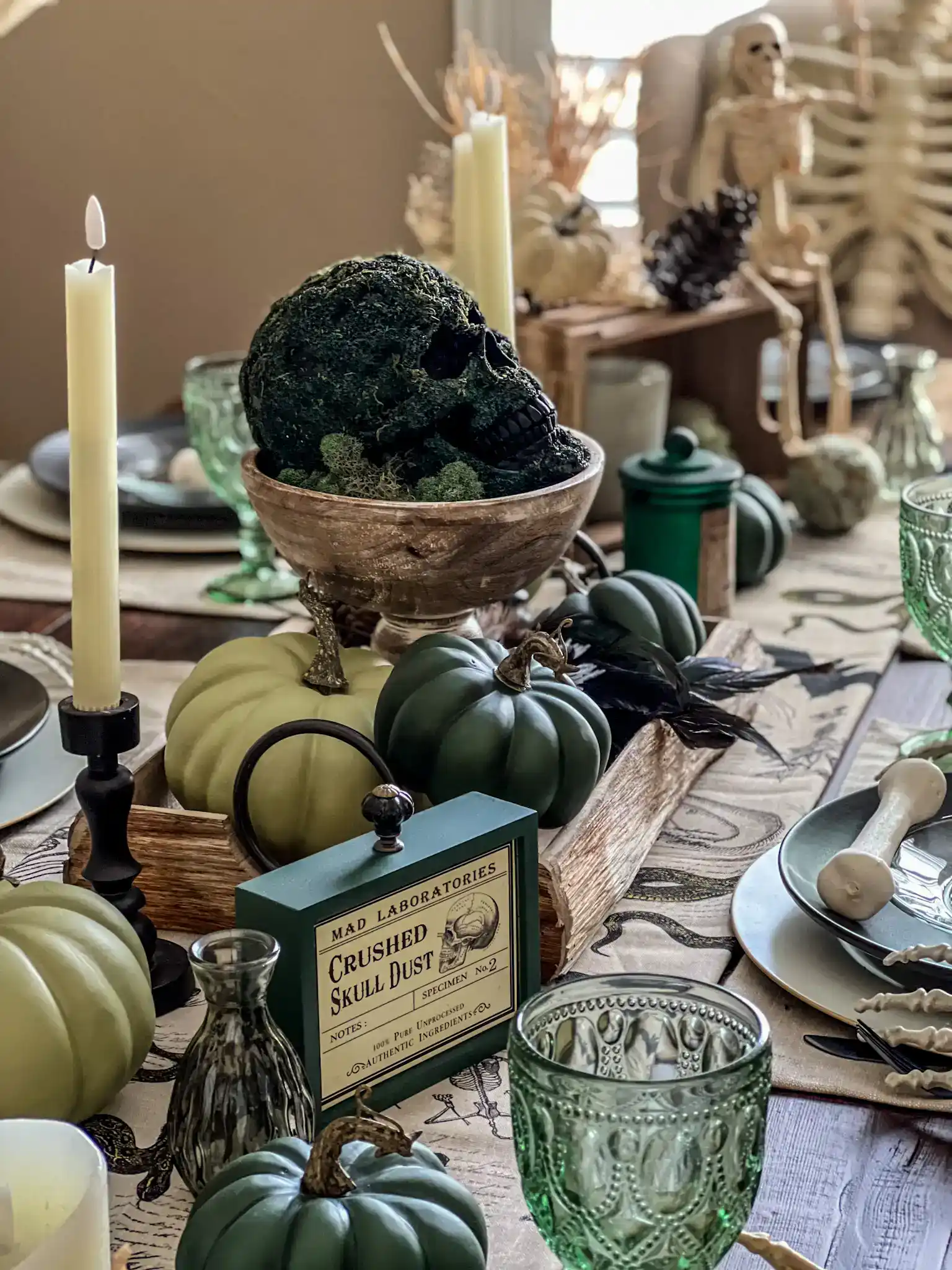 A green and rustic themed Halloween tablescape decor with a skull covered in green moss on a pedestal centerpiece