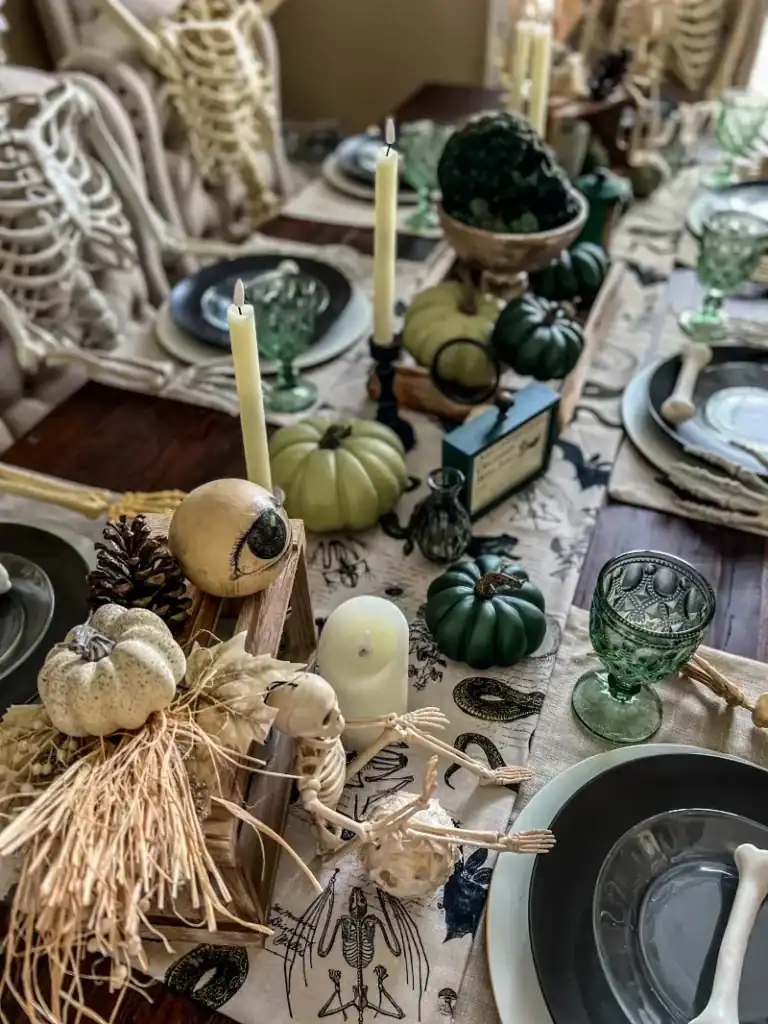 A green white and rustic themed halloween tablescape with pumpkins, skeletons and various green decor items