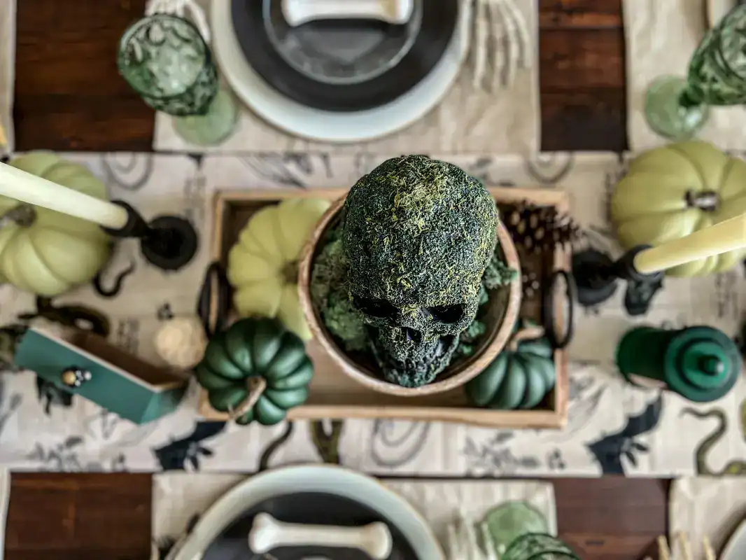 Top view of a skull covered in green moss on a pedestal for a green Halloween tablescape decor