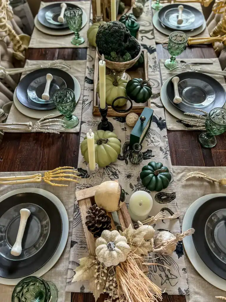 Top view of a green halloween tablescape with items like black plates, moss skull, green and white pumpkins and bones