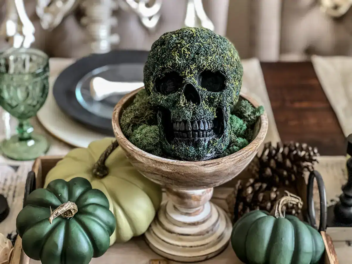 A skull covered in green moss on a pedestal for a green themed Halloween tablescape decor