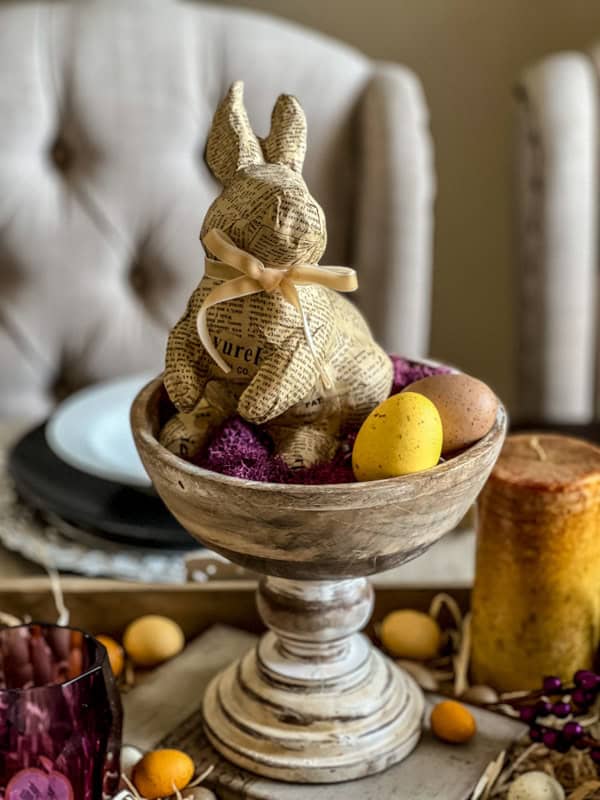 Easter bunny figurine with colorful eggs on a decorative pedestal for spring table decor.