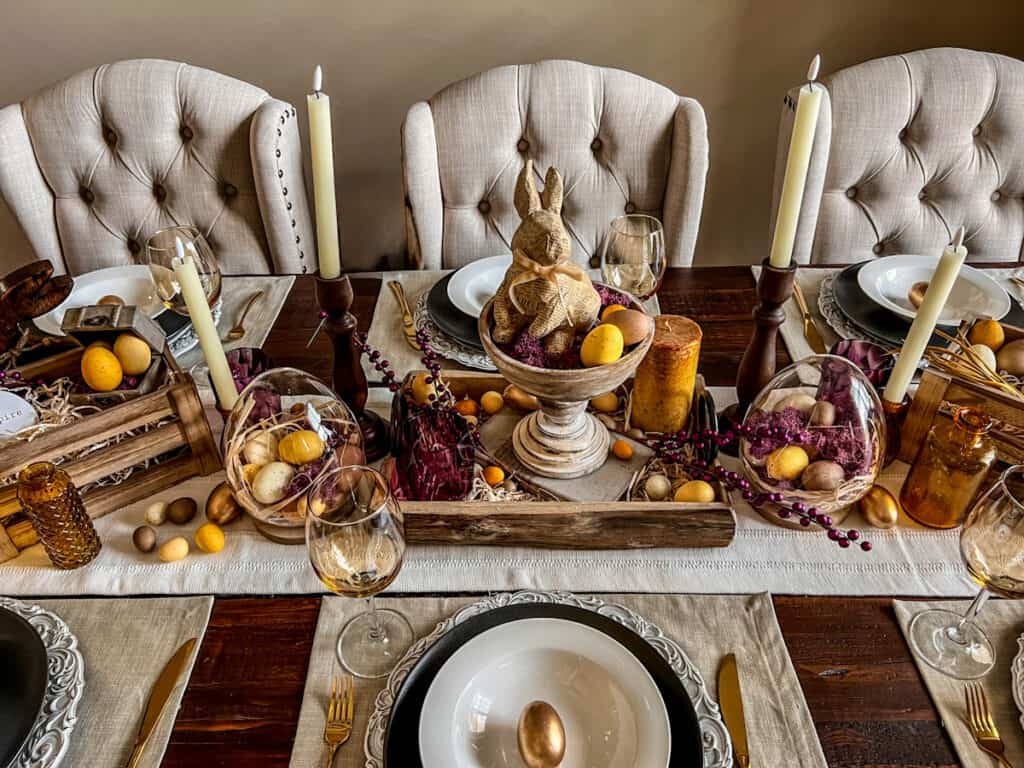 Purple and yellow Easter tablescape with amethyst cups, goldenrod eggs, and a newspaper bunny centerpiece